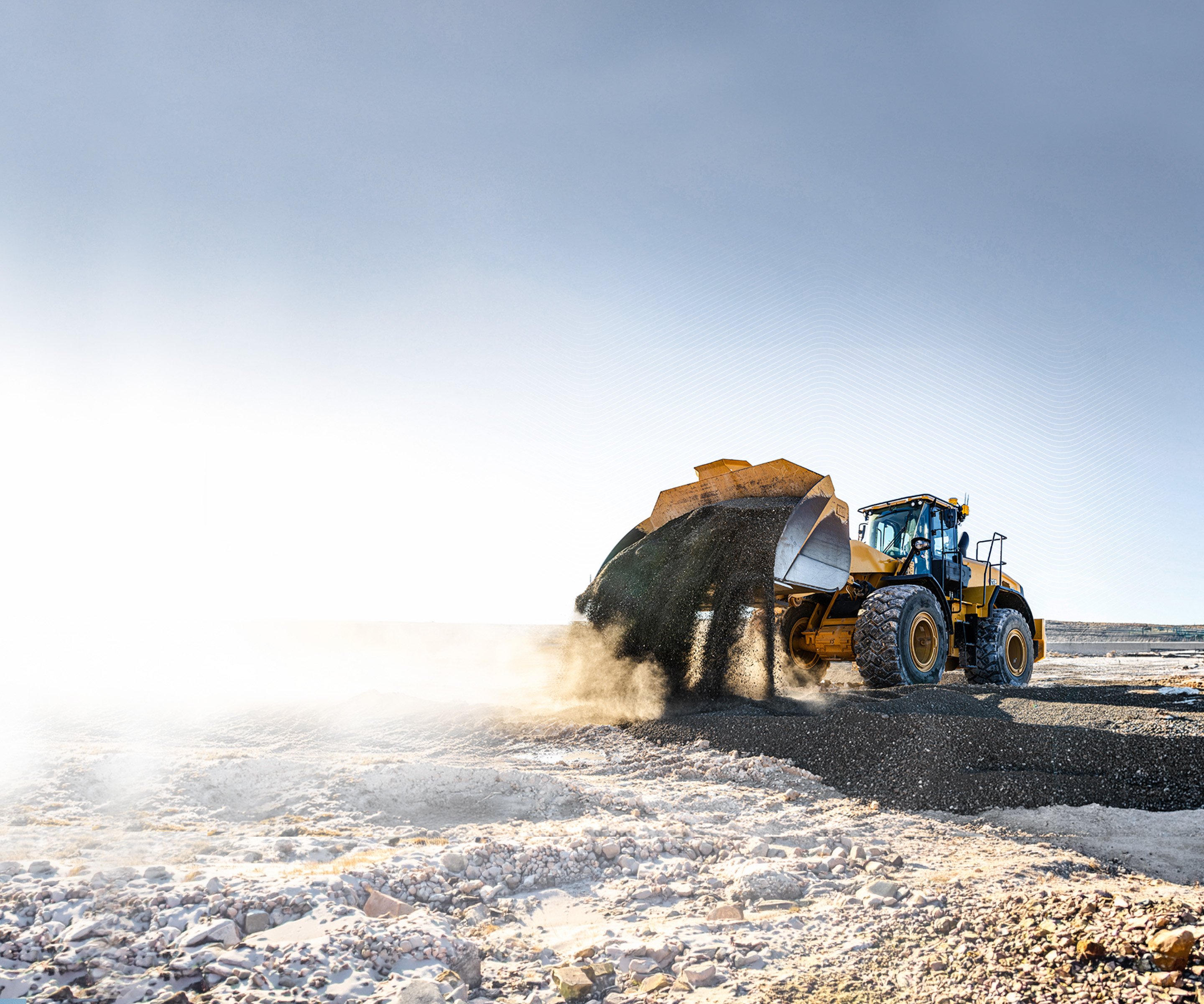 Yellow wheel loader with Trimble GNSS antennas dumping gravel at a sunlit quarry.