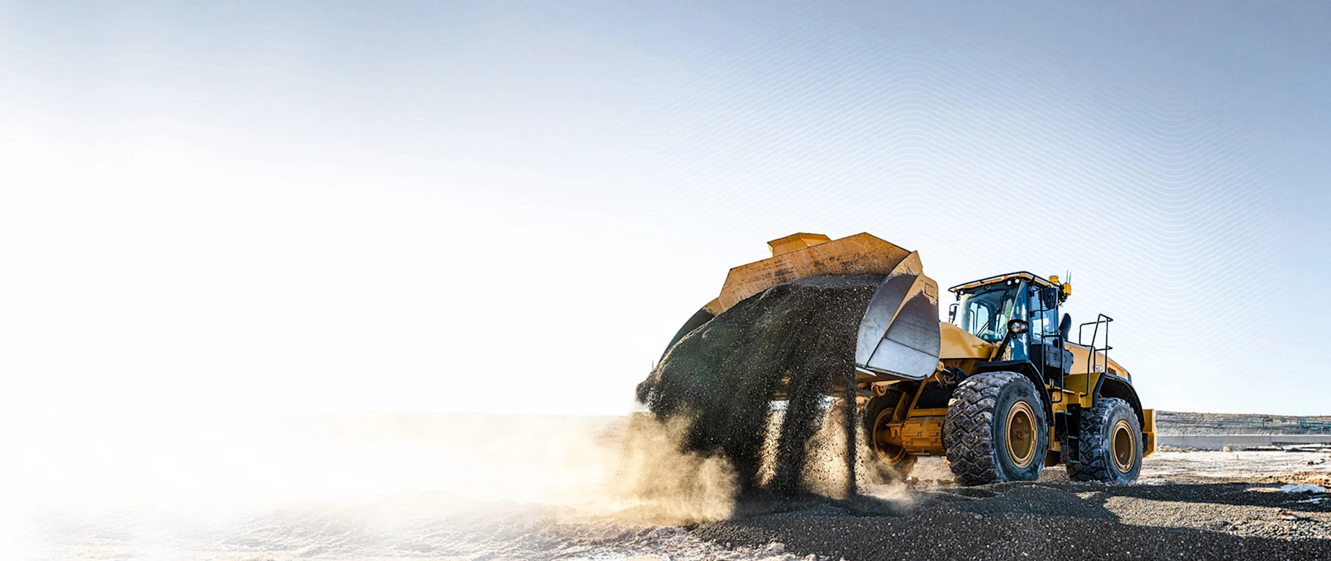 Yellow wheel loader with Trimble GNSS antennas dumping gravel at a sunlit quarry.