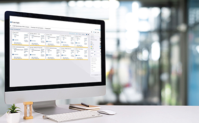 An iMac monitor on a desk in a modern office displays the interface for Trimble ProjectSight, a construction project management software.