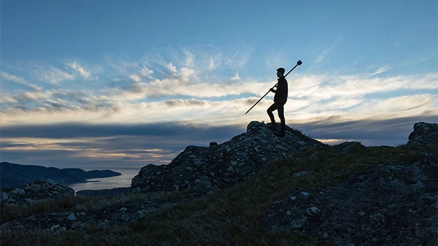 Man using Trimble Geospatial equipment on top of mountain in evening