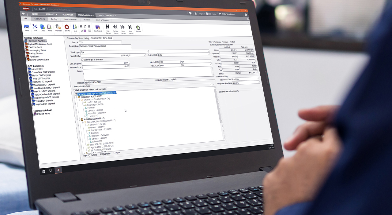 A person uses Trimble's B2W Estimate Enterprise software on a laptop to manage construction project costs and data.