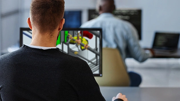 A man viewed from behind looks at a computer screen showing a complex 3D pipe model in Fabrication SmartTools.