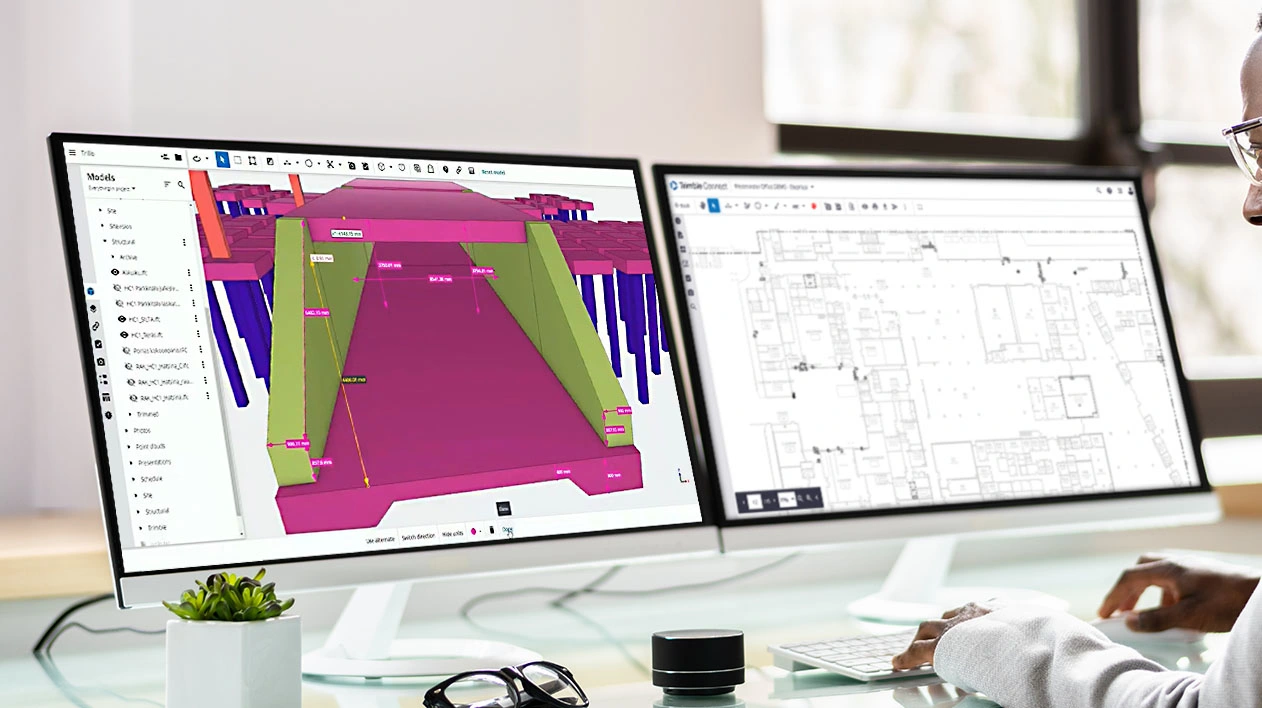 A person uses Trimble Connect on dual monitors to view a 3D structural model and a 2D architectural floor plan.