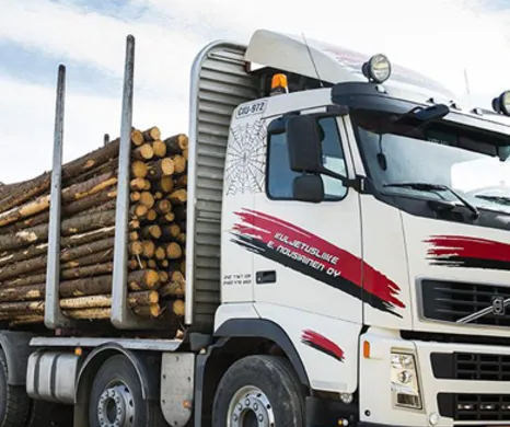 A white Volvo timber truck from Kuljetusliike E. Nousiainen Oy, loaded with logs, utilizing Trimble LogForce software for transport management.