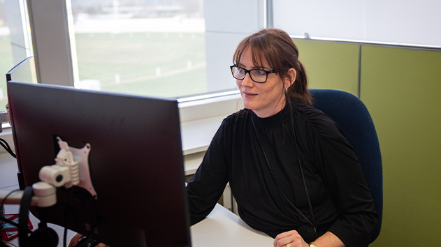 A woman in an office smiles while working at a desktop computer.