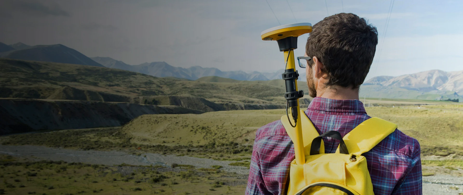 Man using Trimble Geospatial equipment looking at field and mountains
