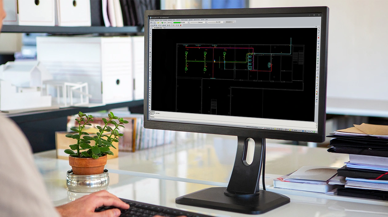 A monitor displaying Stabicad for IntelliCAD software with a 2D MEP layout on a desk.