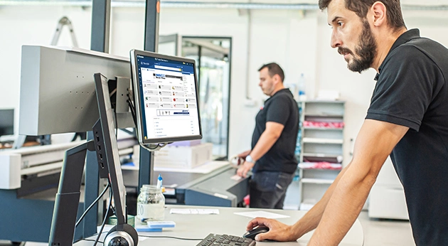 Technicians in a fabrication shop using Trimble’s Tekla PowerFab software on a desktop monitor to manage production workflows.