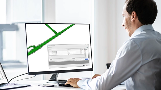 A man works on a computer using Trimble Nova software to design a 3D green piping system with a technical data dialog box open on the screen.