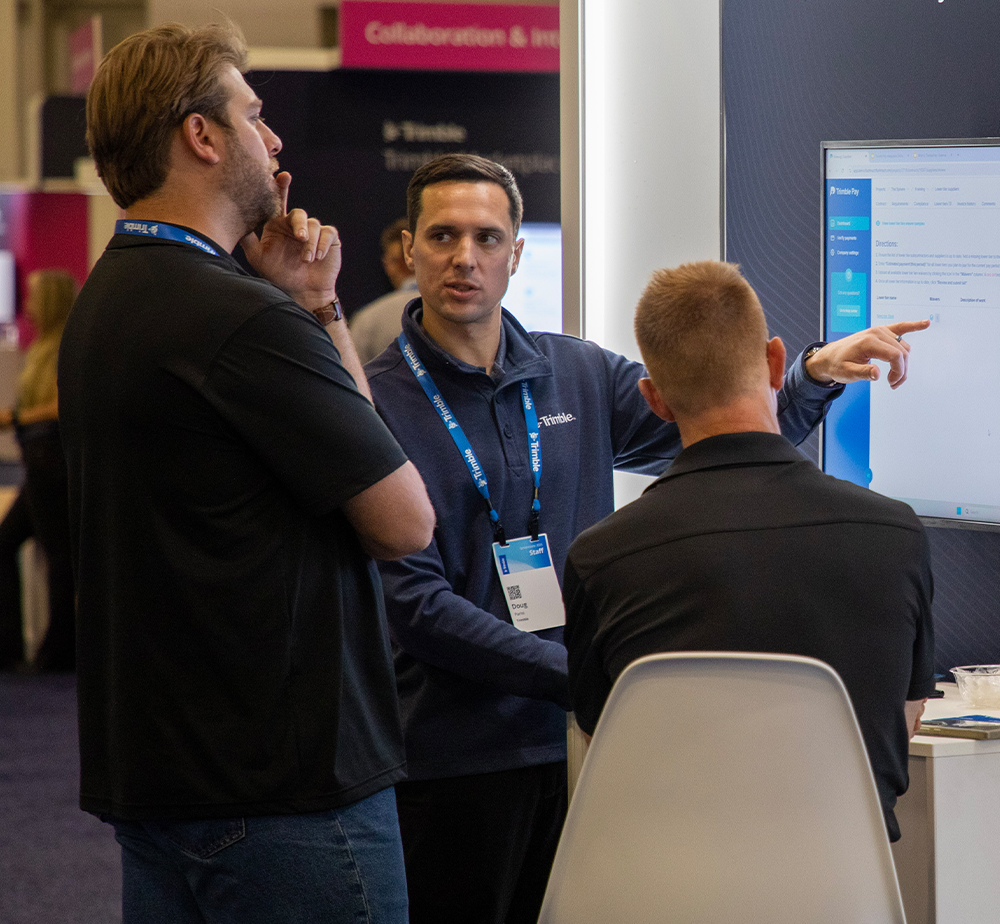 A group of professional attendees discussing a digital display and sharing ideas at the Trimble Dimensions conference.