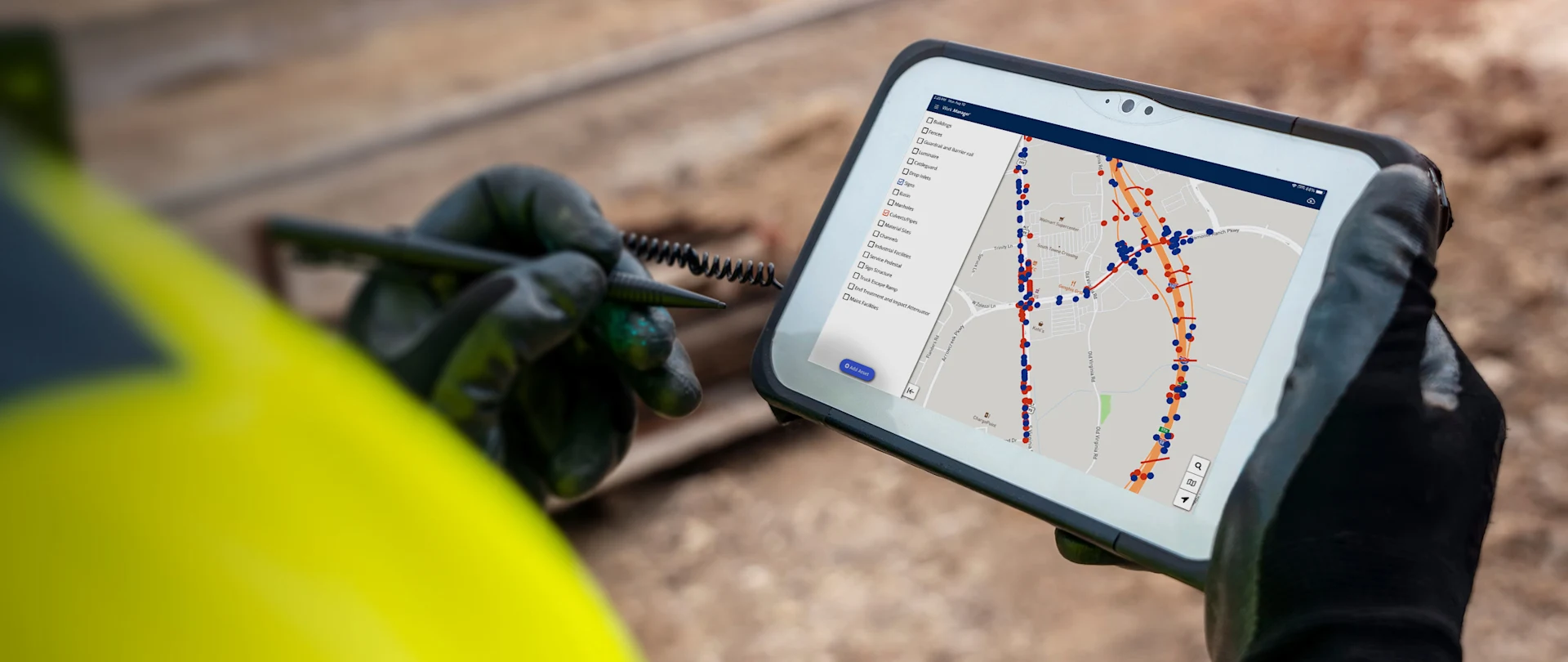 Ein Arbeiter mit Handschuhen und Schutzhelm hält ein Tablet, auf dem die Trimble-Software eine Karte mit markierten Routen anzeigt.