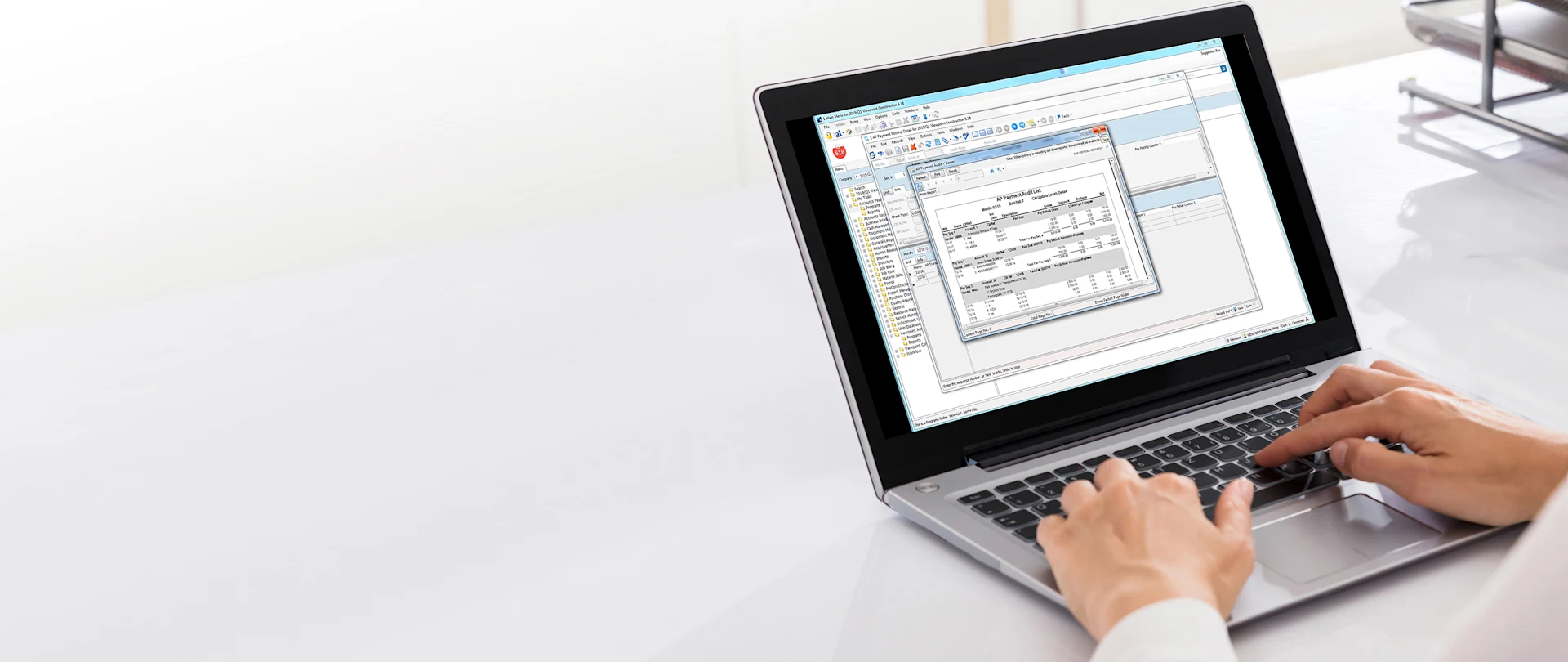 A person uses a laptop running Trimble Viewpoint construction software to review an AP payment audit report.