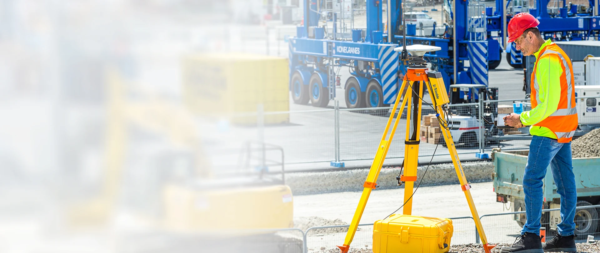 Surveyor on a construction jobsite with machinery behind them, standing next to the Trimble R750 Model 2 modular GNSS receiver mounted on a tripod with an antenna.