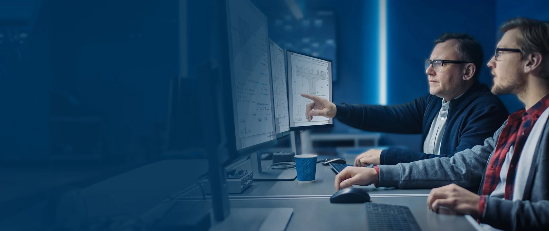 Two professionals collaborate in an office, reviewing structural drawings on multiple monitors using Trimble Tekla software.