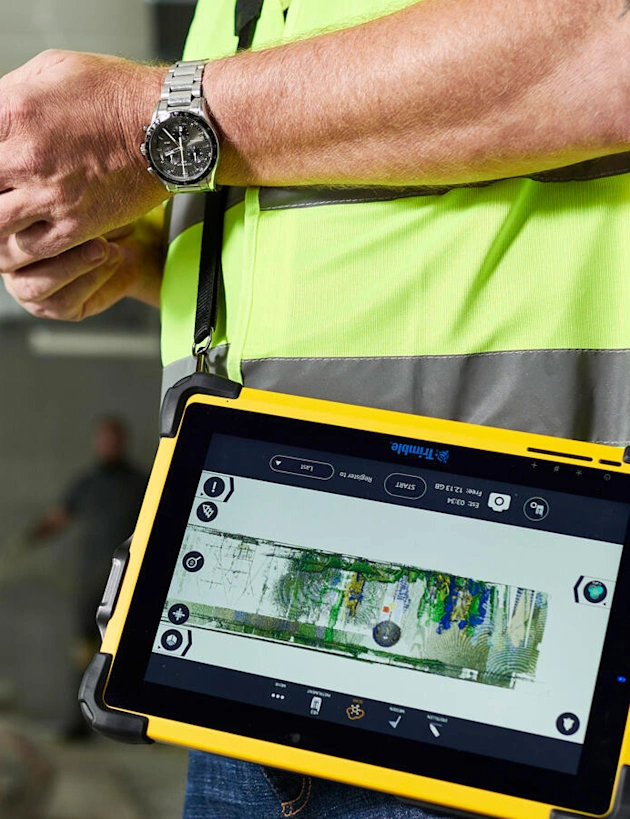 A worker uses a Trimble rugged tablet and FieldLink software to review a 3D point cloud scan on a construction site.
