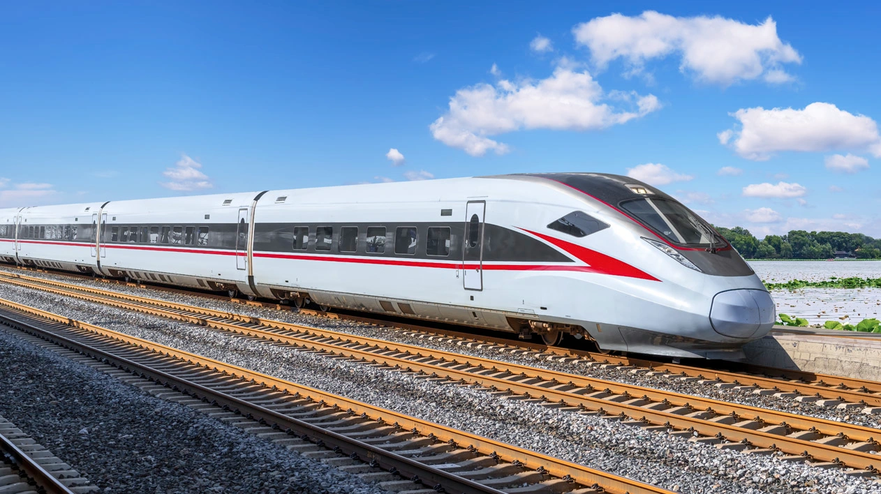 A white high-speed train with red accents is moving on a track under a blue sky with scattered clouds.