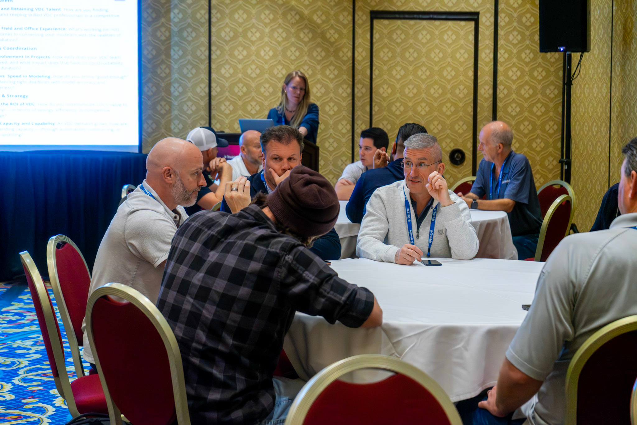 Attendees network with each other in small groups at tables inside of a breakout session room.