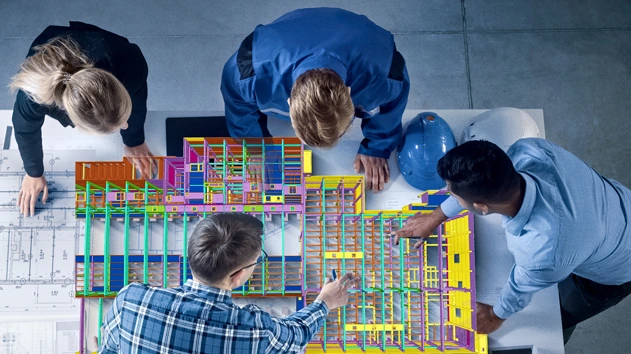 Four engineers collaborate around a colorful 3D building model and blueprints, utilizing Trimble's BIM and structural detailing software.