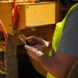 A worker in a high-visibility vest uses a Trimble handheld data collector on a job site with heavy construction machinery in the background.