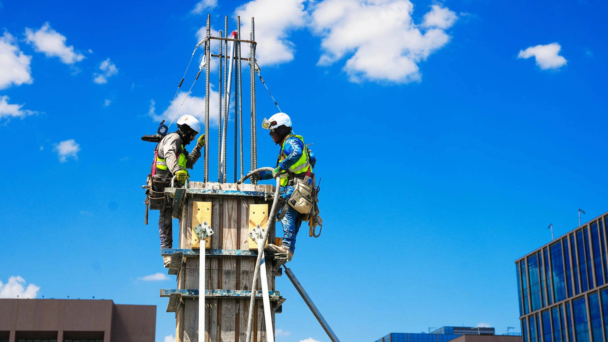 Two JE Dunn workers pouring concrete into a column mold, ensuring proper placement and finish.