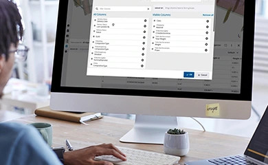 A person works at a desk with a monitor displaying a Trimble software interface, featuring a column management dialog for BIM data.