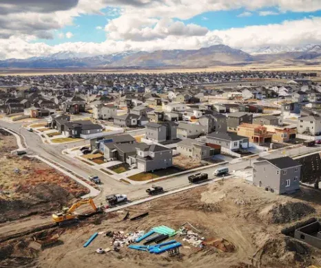 Luchtfoto van woningbouw in Utah met een gele graafmachine en moderne huizen voor een decor van besneeuwde bergen.