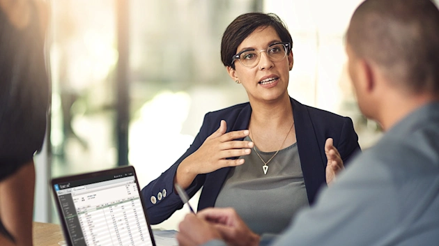 Woman actively discussing, gesturing towards a laptop displaying Trimble's Viewpoint Spectrum construction management software, showing project financial data for AECO insights.