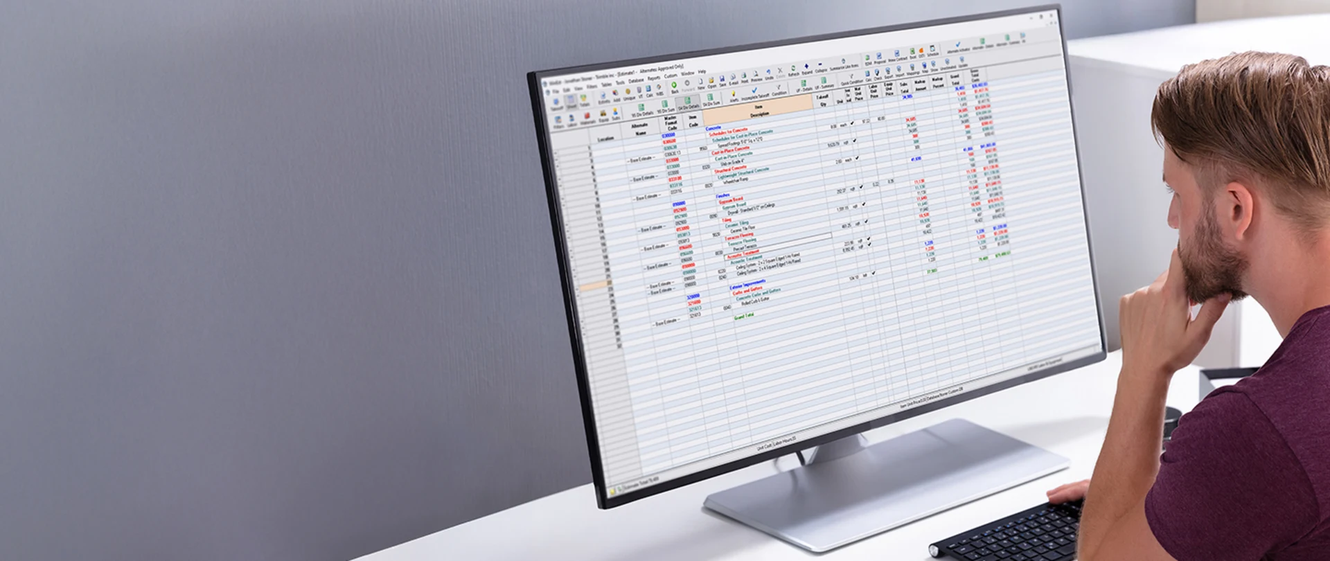 A man reviews a construction estimate in Trimble WinEst software on a large desktop monitor.