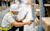 A warehouse worker in a hard hat and safety vest uses a rugged tablet and handheld scanner to check inventory on a shelf.