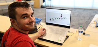 Young adult working on laptop in classroom looking back and smiling at camera