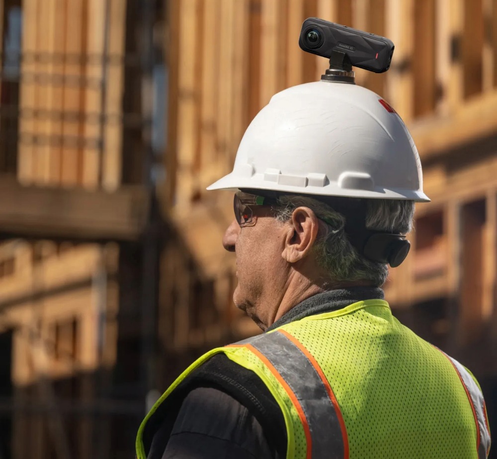 Construction worker with high-vis yellow vest and PPE wearing a hard hat with an Insta360 Camera attached on top via a mount.