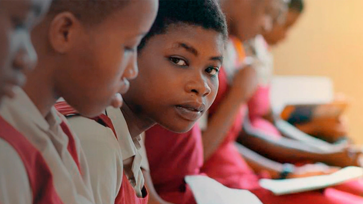 Female students wearing red sitting in classroom while holding papers