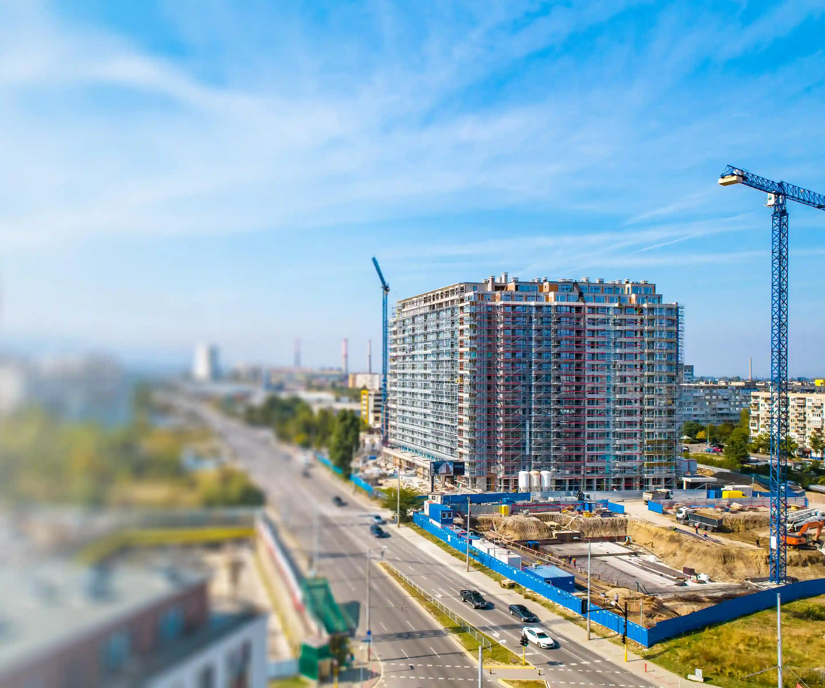 Tilt-shift foto van een gebouw in aanbouw in Sofia, Bulgarije, met blauwe kranen, steigers en industriële schoorstenen.