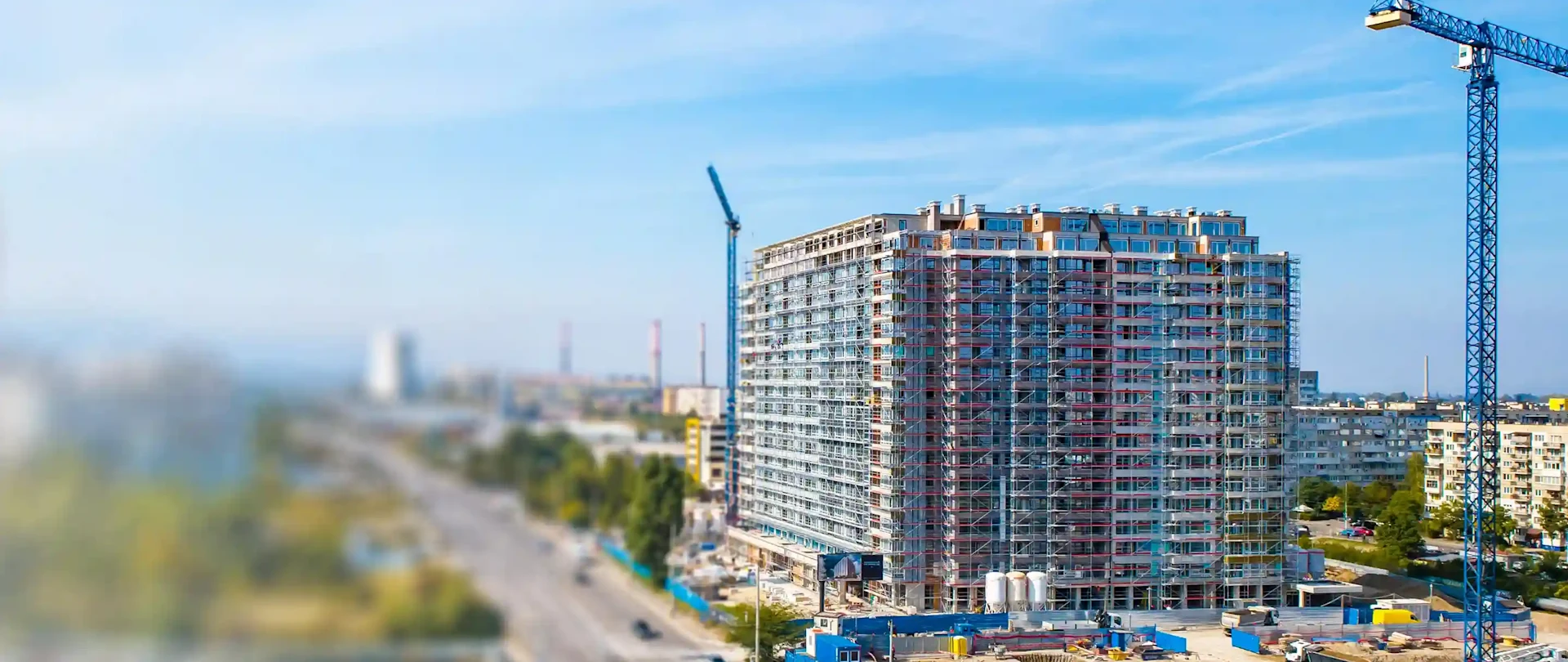 Tilt-shift foto van een gebouw in aanbouw in Sofia, Bulgarije, met blauwe kranen, steigers en industriële schoorstenen.