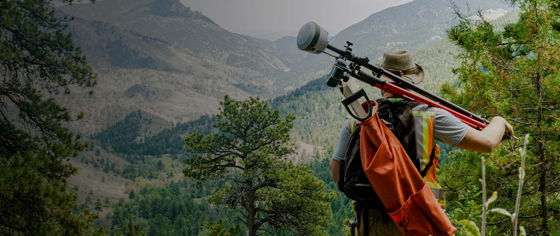 Man holding Trimble Geospatial equipment looking at trees on mountains