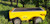 A small, bright yellow autonomous robot with a large solar panel on its top is positioned amidst rows of grapevines, partially obscured by the green foliage.