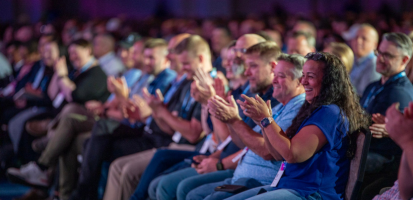 Dimensions attendees laugh and clap in the audience of the keynote presentation.
