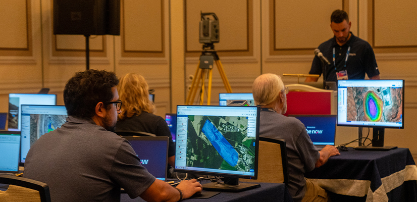 Attendees at a Trimble Dimensions training session use desktop computers to analyze mapping data and geospatial models.