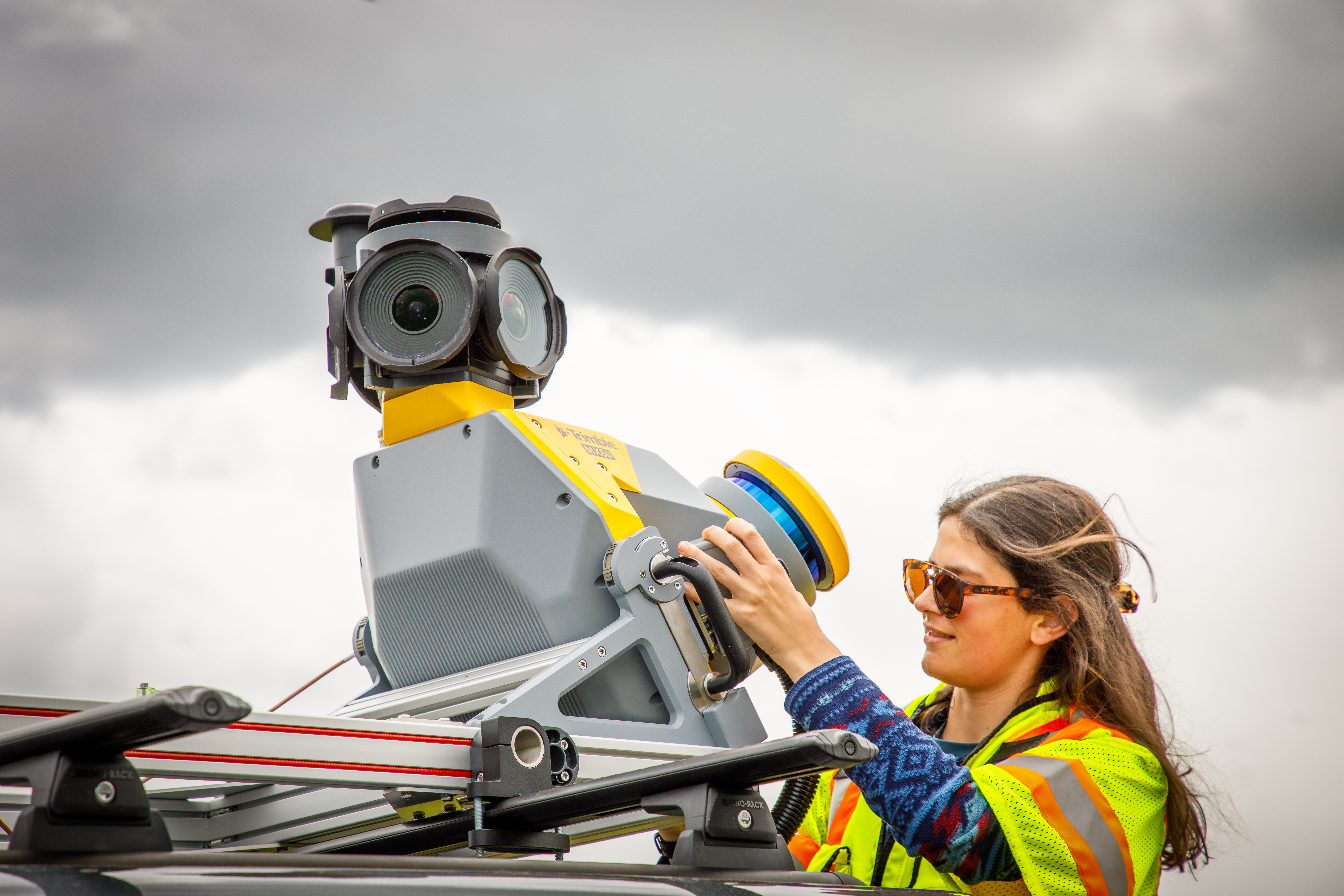 A technician in a safety vest adjusts a Trimble MX60 mobile mapping system mounted on a vehicle roof.
