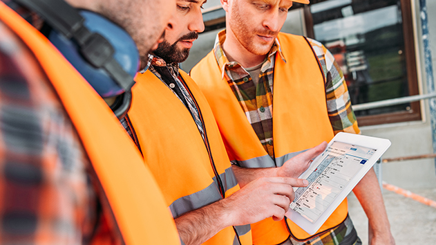 Team of construction workers in safety vests collaborating on digital project management via a tablet.