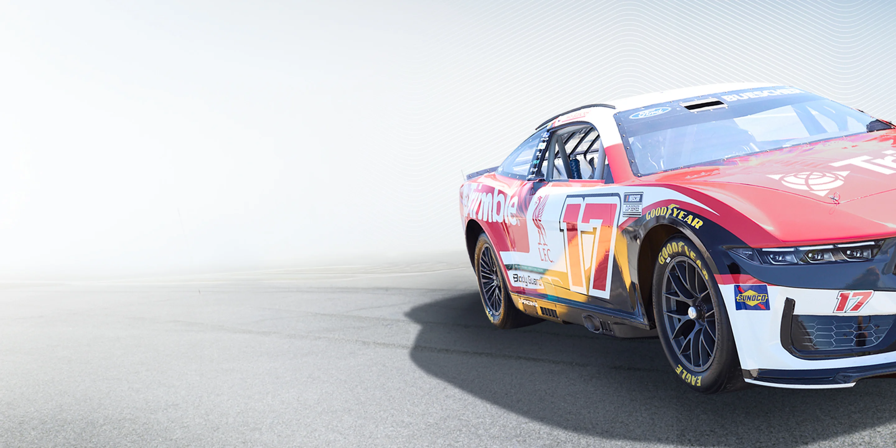 Chris Buescher's #17 Trimble (AECO tech) & Liverpool FC NASCAR Ford Mustang Dark Horse. Red/white/black livery, Liverpool Bird, blurred track.