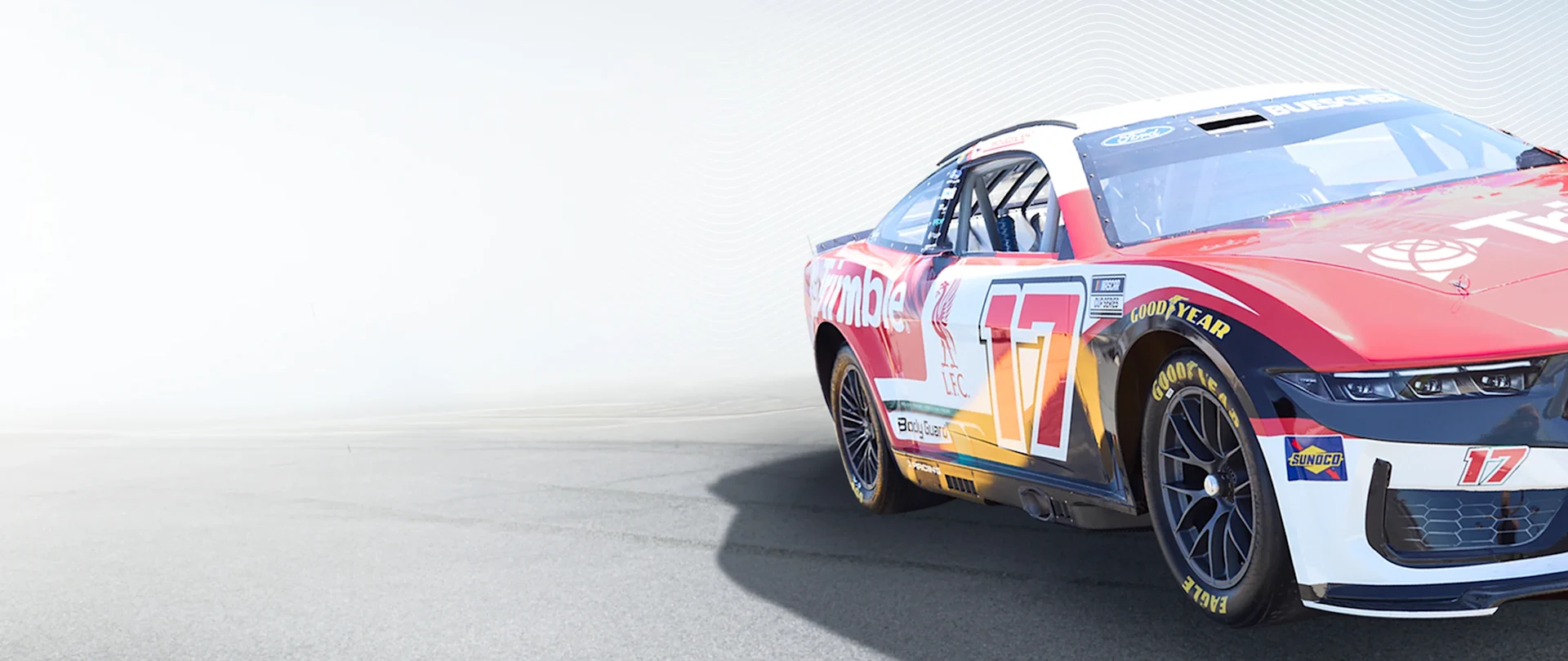 Chris Buescher's #17 Trimble (AECO tech) & Liverpool FC NASCAR Ford Mustang Dark Horse. Red/white/black livery, Liverpool Bird, blurred track.
