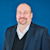 Headshot of Peter Large, SVP of Trimble, smiling in a blue and white shirt against a solid blue background.