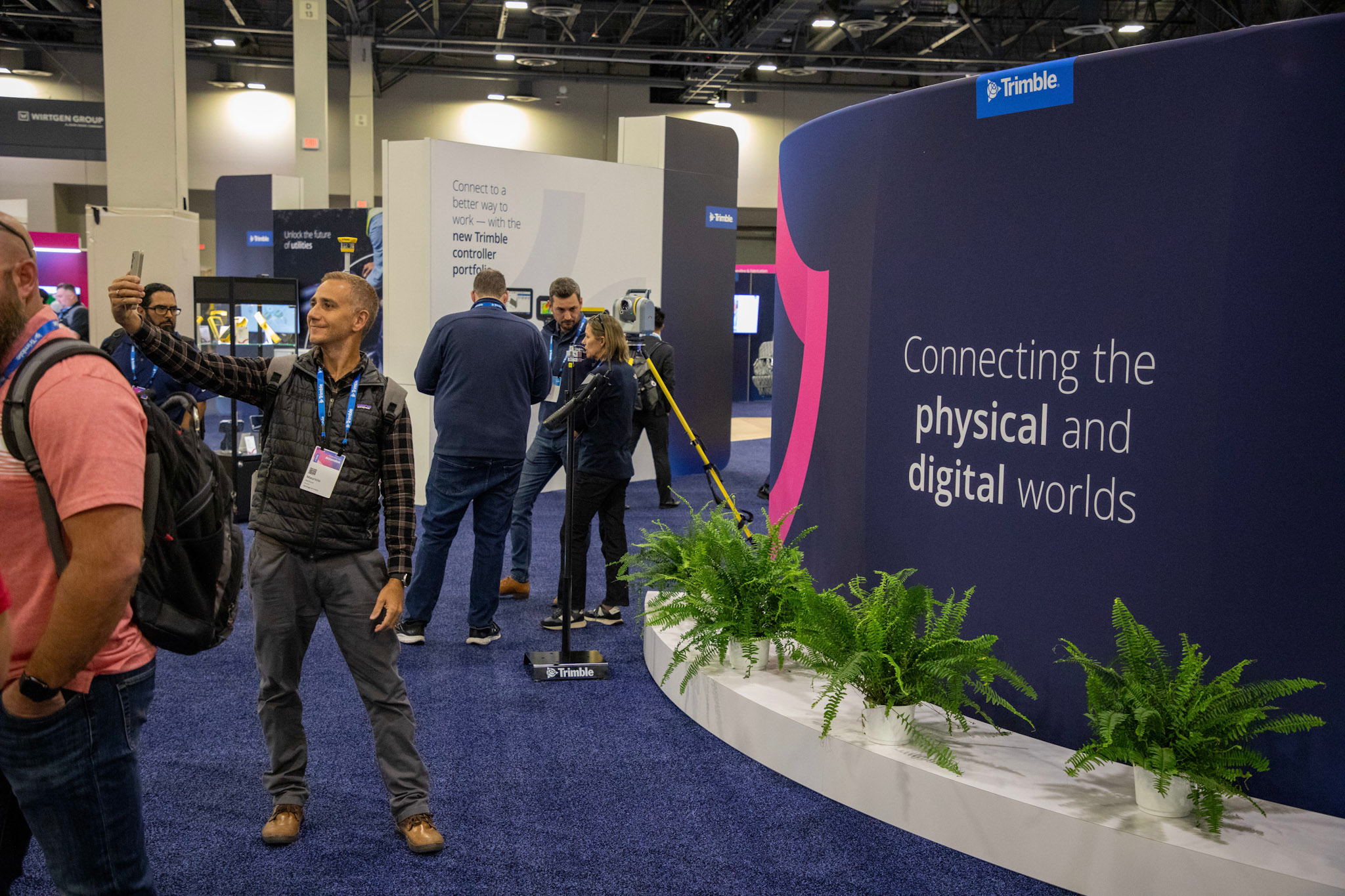 An attendee stops to take a selfie with some of the Trimble branding in the Expo Hall at The Venetian Resort while others network in the background.