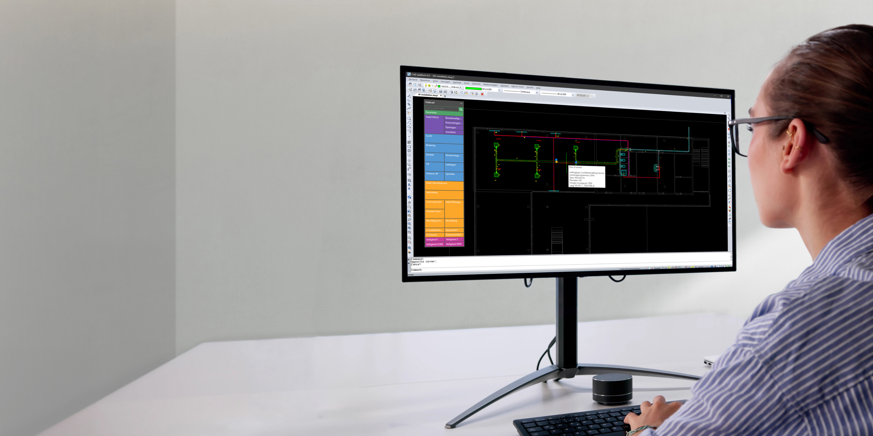 Een vrouw in een gestreept shirt gebruikt Stabicad LT-software op een groot scherm om MEP-systemen te ontwerpen in een lichte, moderne kantooromgeving.