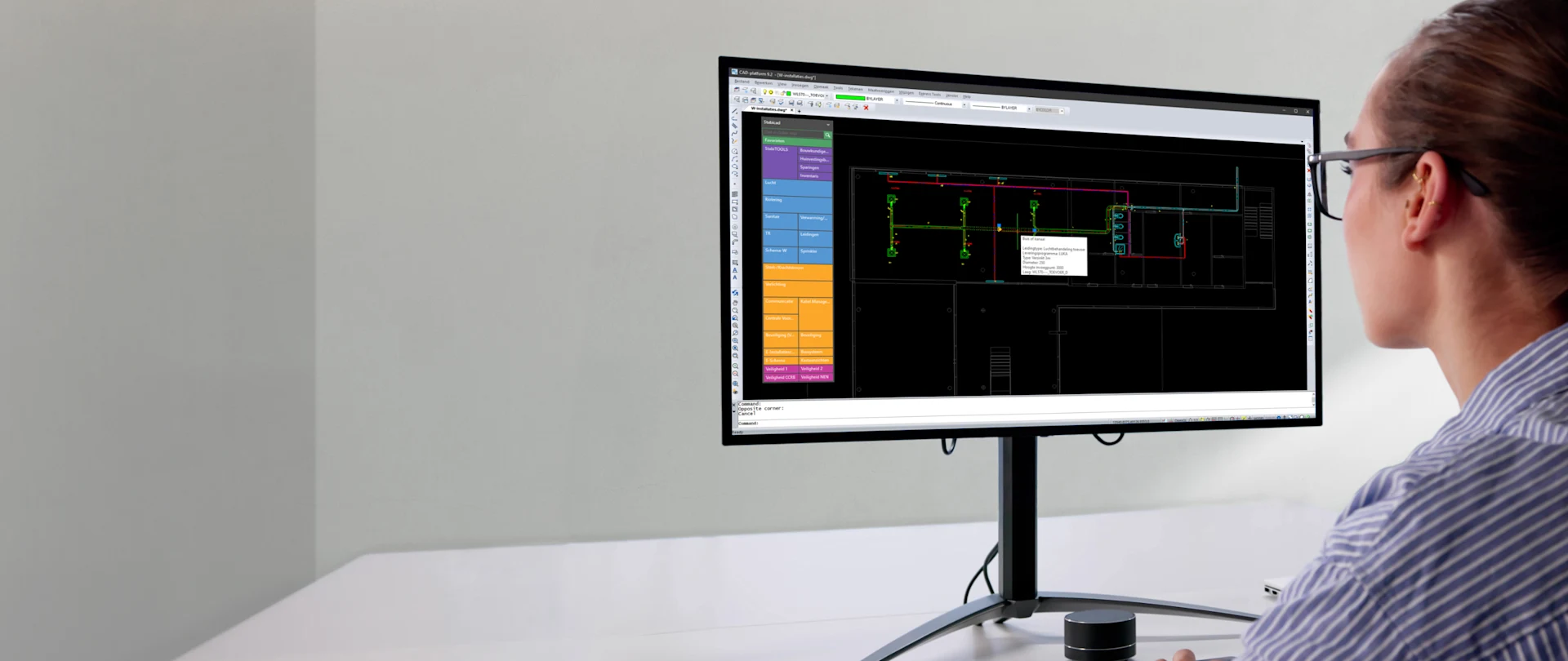 A woman in a striped shirt uses Stabicad LT software on a large monitor to design MEP systems in a bright, modern office setting.