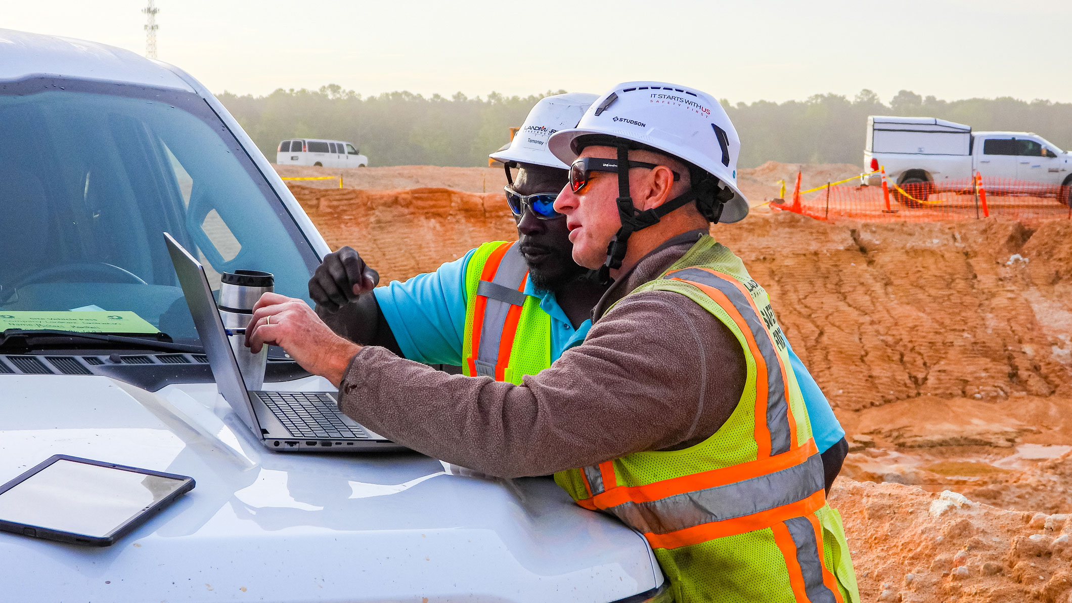 Landmark Construction operator and a colleague review Trimble software on a laptop and tablet at a construction site.