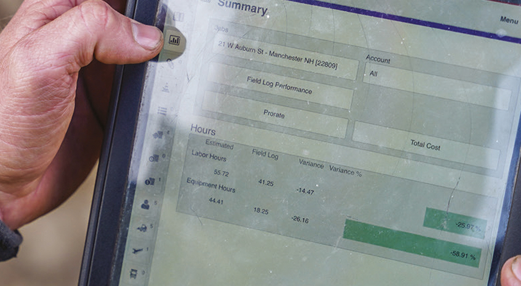 Hands hold a tablet displaying a Trimble B2W Track summary page for a construction project in Manchester, NH, showing hour variances.
