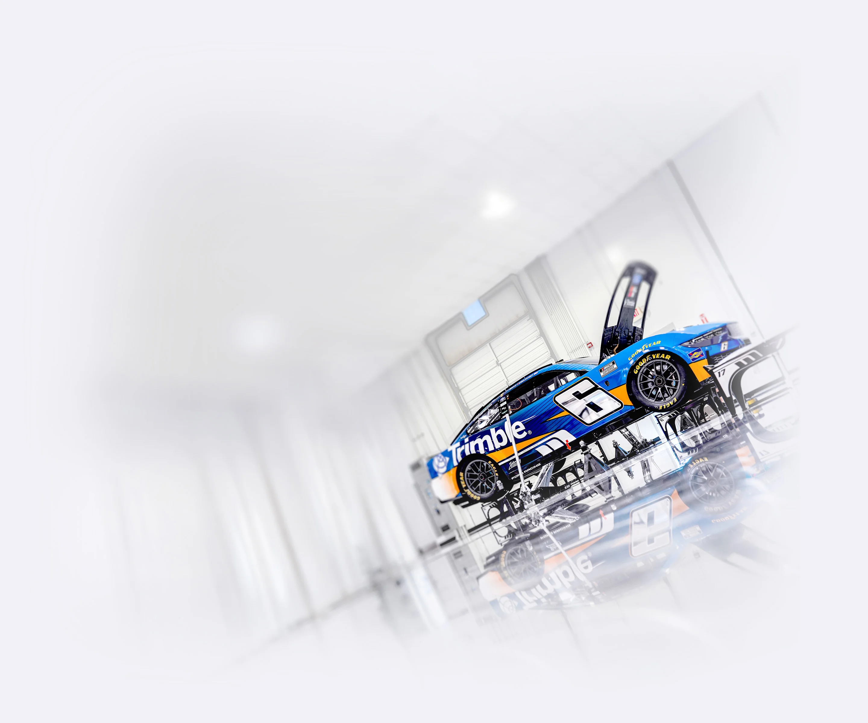 The No. 6 Trimble Ford Mustang for RFK Racing with its hood open, reflected on a glossy floor in a sleek, white studio.