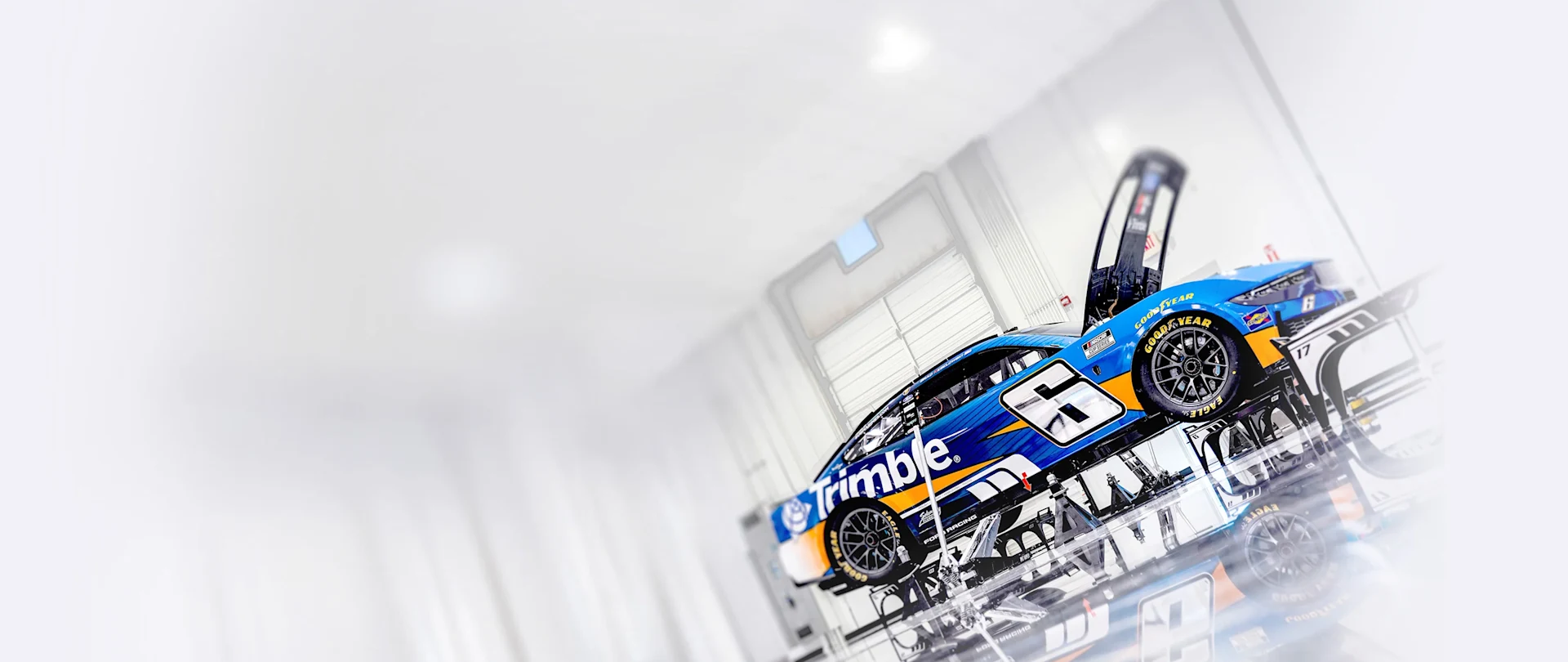 The No. 6 Trimble Ford Mustang for RFK Racing with its hood open, reflected on a glossy floor in a sleek, white studio.